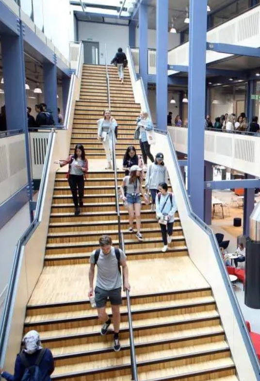 Students walk down stairs in grand hall of building on university campus
